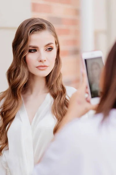 Uma mulher bonita em roupas brancas é fotografada no telefone para redes sociais. — Fotografia de Stock