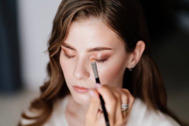 Uzun saçlı güzel bir kadın düğün ya da fotoğraf çekimi için makyaj yapıyor.