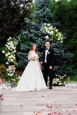 Yaşayan çiçeklerle dolu bir kemerde açık hava düğün töreni. Güzel bir çift yeni evli.