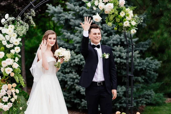 Trauung in einem Bogen lebender Blumen. Frischvermählte zeigen Hände mit Ringen — Stockfoto