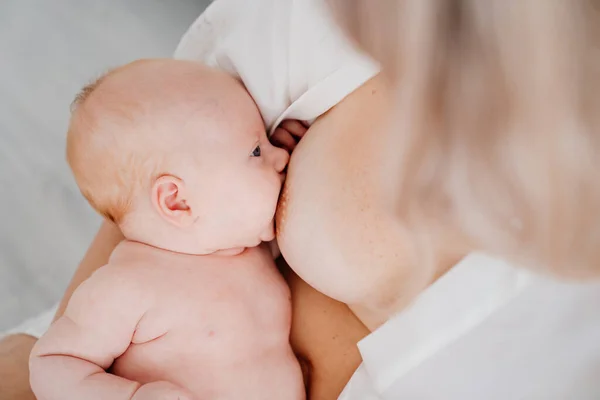 De cerca. mujer está acostada con un bebé en una cama blanca alimentando con leche materna. — Foto de Stock