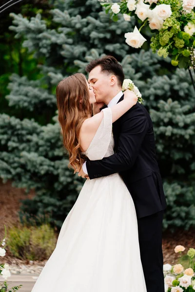 Cérémonie de mariage en arc de fleurs vivantes.Beaux jeunes mariés embrassant doucement — Photo