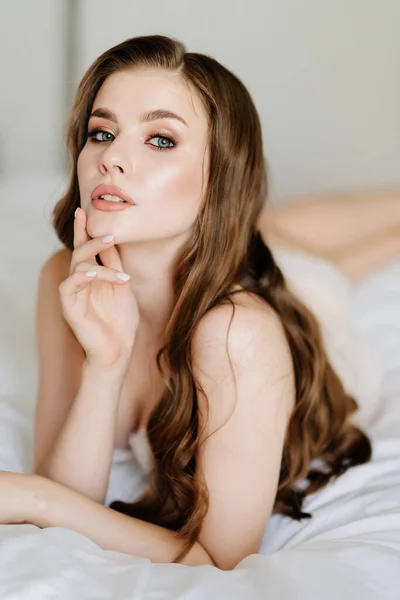 De cerca. retrato de mujer hermosa con el pelo largo en ropa interior acostado en la cama. — Foto de Stock