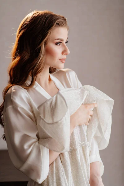 Retrato de mulher bonita em roupão branco segurando vestido de noiva na frente dela — Fotografia de Stock