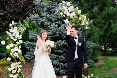 Canlı çiçeklerle dolu bir kemerde düğün töreni. Yeni evliler yüzüklerle el ele tutuşur.