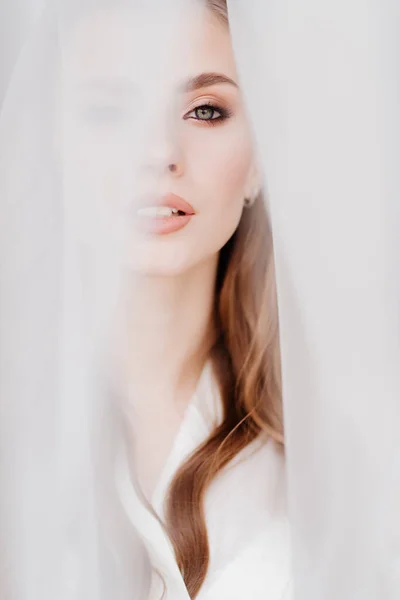 Porträtt av en vacker ung kvinna i en vit morgonrock under en bröllopsslöja. — Stockfoto