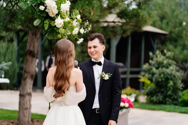 Cerimonia nuziale in arco di fiori vivi. lo sposo ascolta il voto delle spose — Foto Stock
