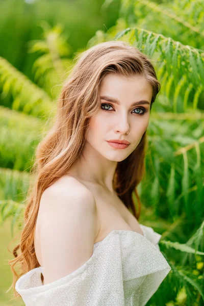 Retrato de una hermosa mujer en un vestido blanco contra el de hojas verdes. —  Fotos de Stock