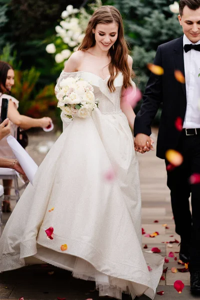 De beaux jeunes mariés vont à la cérémonie de mariage en plein air dans une arche de fleurs vivantes — Photo