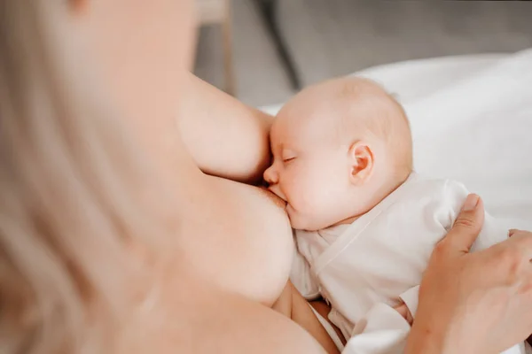 De cerca. mujer está acostada con un bebé en una cama blanca alimentando con leche materna. —  Fotos de Stock