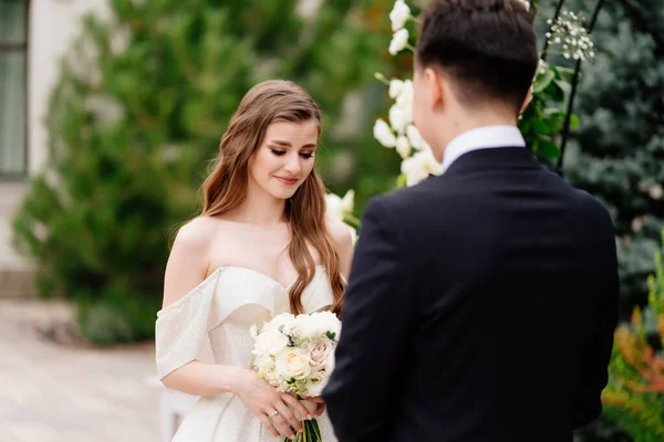 Hochzeitszeremonie im Bogen der Blumen. Braut hört auf das Gelübde und die Schreie der Bräutigame. — Stockfoto