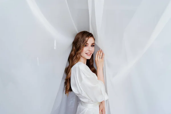 Красивая молодая женщина с длинными волосами в белом халате стоит под занавесом — стоковое фото