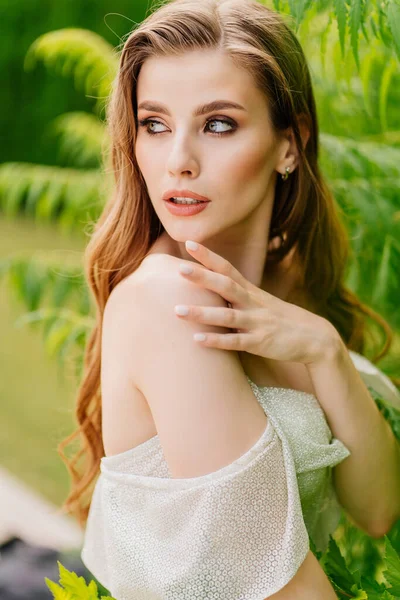 Retrato de una hermosa mujer en un vestido blanco contra el de hojas verdes. — Foto de Stock