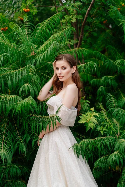 Красивая женщина в белом платье, позирующая на фоне зеленых листьев. — стоковое фото