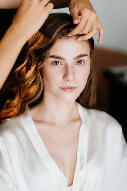 Uzun saçlı güzel bir kadın düğün ya da fotoğraf çekimi için kuaförlük yapıyor.