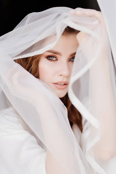 Retrato de una hermosa joven con una túnica blanca bajo un velo de boda. — Foto de Stock