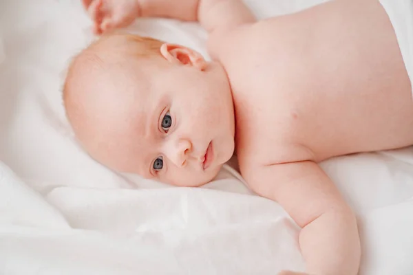 Lindo bebé de pelo rojo se encuentra en una cama blanca. concepto de cuidado del bebé — Foto de Stock