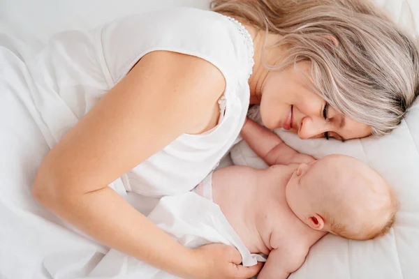 Mamá es mamá está acostada con un bebé en una cama blanca después de alimentar a la leche materna. — Foto de Stock