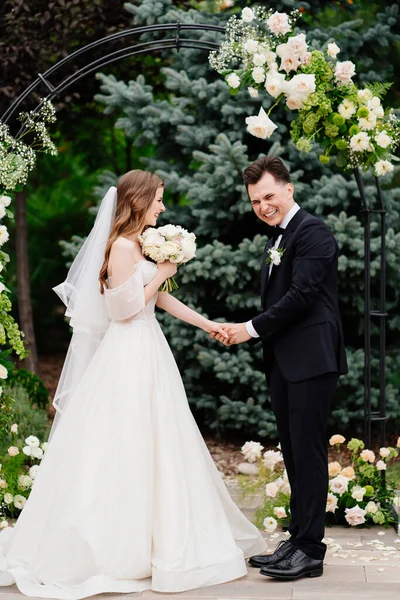 Trauung im Freien in einem Bogen lebender Blumen. Frischvermählte halten Händchen — Stockfoto