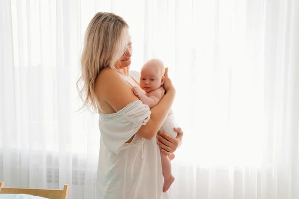 Mamá con el bebé de pie en la ventana. después de la lactancia. — Foto de Stock