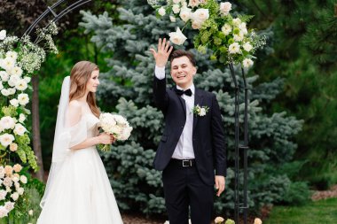 Canlı çiçeklerle dolu bir kemerde düğün töreni. Yeni evliler yüzüklerle el ele tutuşur.