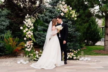 Yaşayan çiçeklerin kemerinde düğün töreni. Güzel yeni evliler şefkatle kucaklaşır.