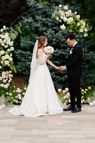 Buiten huwelijksceremonie in een boog van levende bloemen. pasgetrouwden houden elkaars hand vast — Stockfoto