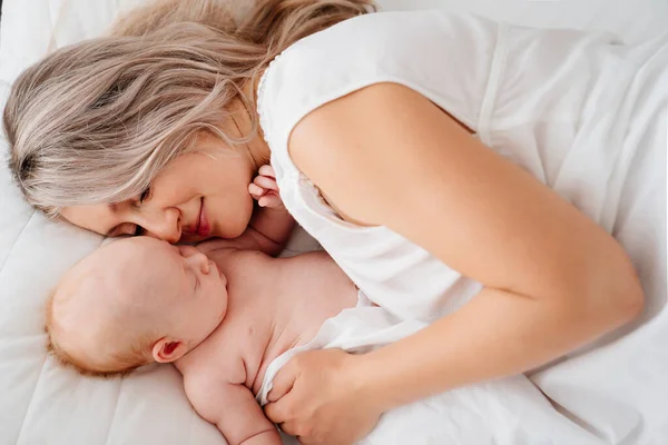 Mamá es mamá está acostada con un bebé en una cama blanca después de alimentar a la leche materna. —  Fotos de Stock