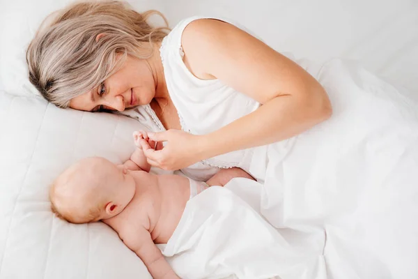 Mama este mama este culcat cu un copil într-un pat alb după hrănirea laptelui matern . — Fotografie, imagine de stoc
