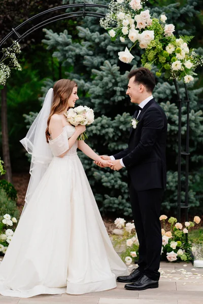 Cérémonie de mariage en plein air dans une arche de fleurs vivantes. jeunes mariés se tiennent la main — Photo