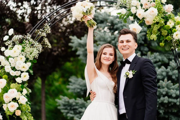Hochzeitszeremonie im Freien in einem Bogen lebender Blumen.Schönes Brautpaar — Stockfoto