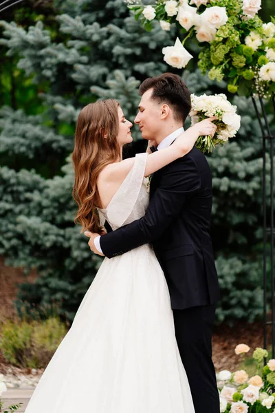 Cérémonie de mariage en arc de fleurs vivantes.Belles jeunes mariés embrassent tendrement — Photo