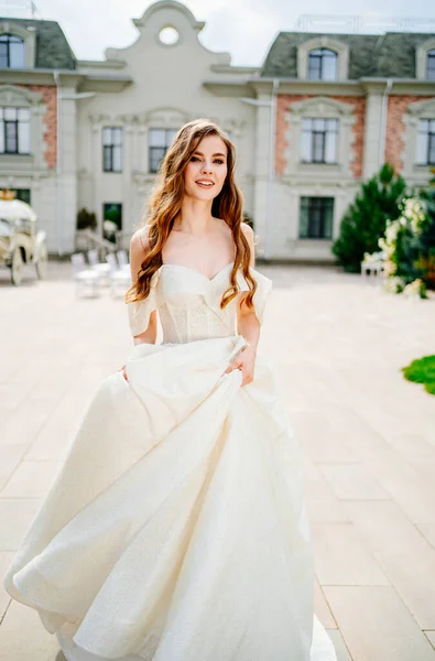 Alegre hermosa mujer en vestido de novia blanco gira cerca de hermoso edificio. — Foto de Stock