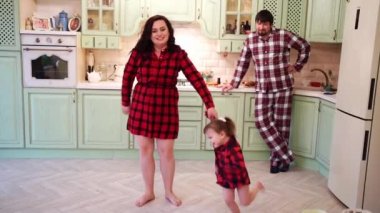Mutlu bir aile. Anne ve kızı mutfakta oynayıp dans ediyor ve baba onları izliyor..