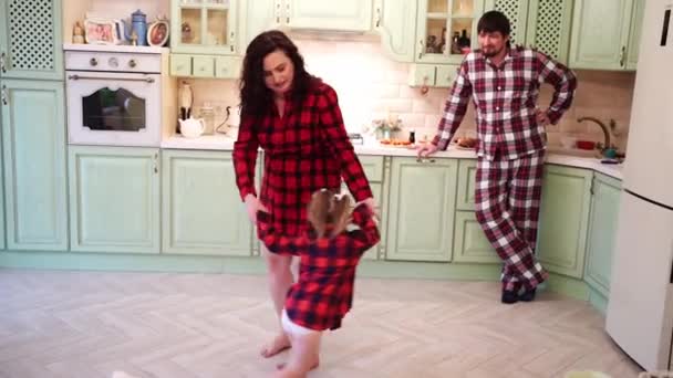 Familia feliz. Mamá y su hija juegan y bailan en la cocina, y papá los observa.. — Vídeo de stock