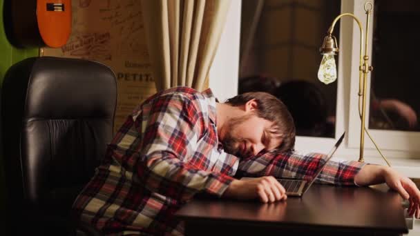 En man i röd rutig pyjamas arbetade sent vid datorn och somnade. — Stockvideo