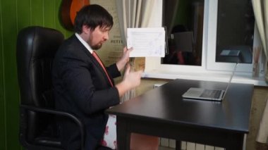 Pantolonlu, ceketli ve kravatlı bir adam grafik çiziyor ve online bir konferansa liderlik ediyor.