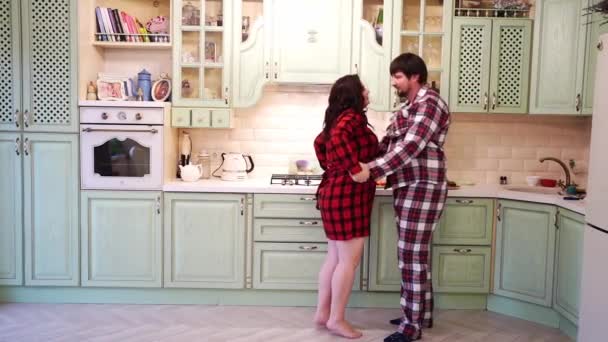 Mam en pap in pyjama knuffelen en kussen in de keuken. Een kind komt aanrennen. — Stockvideo