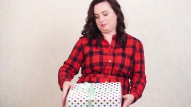 Kırmızı kareli elbiseli bir kadın paketlenmiş bir hediye taşıyor..