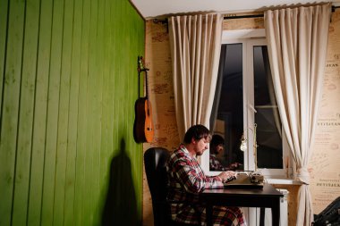 Ekose pijamalı bir adam gece kendi ofisinde daktilo kullanıyor..