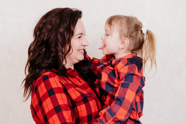 Mutter hält sich in den Armen und kuschelt mit ihrer kleinen Tochter in rot karierten Kleidern. — Stockfoto