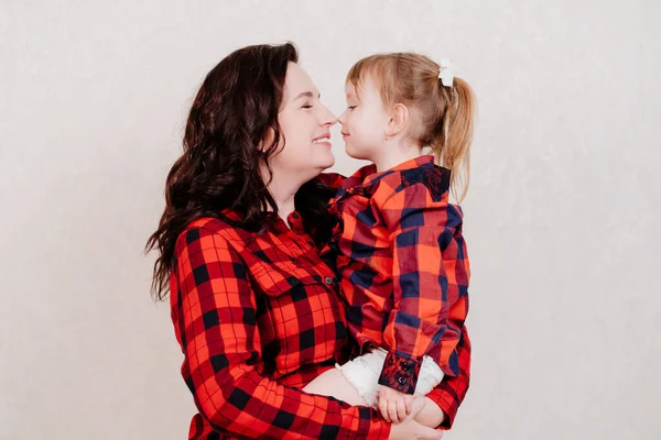 Mutter hält sich in den Armen und kuschelt mit ihrer kleinen Tochter in rot karierten Kleidern. — Stockfoto