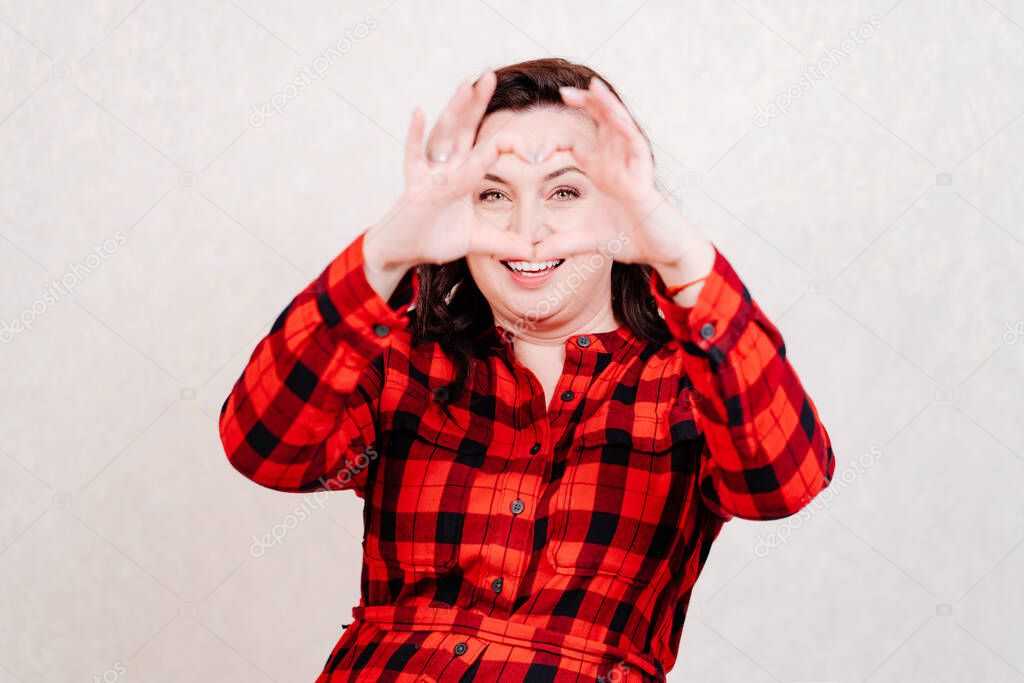 Attractive brunette woman in red dress folded her fingers into heart shapes