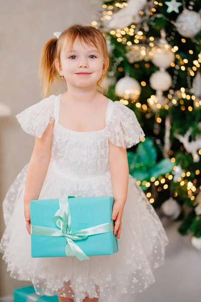 Menina feliz em um vestido branco com caixas de presentes perto da árvore de Natal — Fotografia de Stock