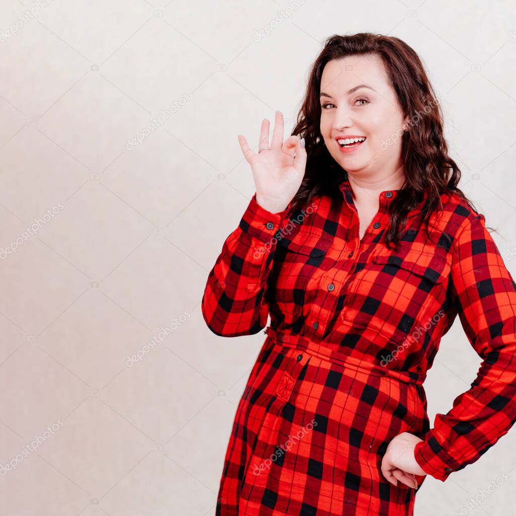 Attractive brunette woman in red dress folded her fingers the ok sign. 