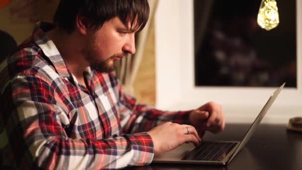 Facet w czerwonej piżamie pisze tekst, pracuje na komputerze. praca zdalna. — Wideo stockowe