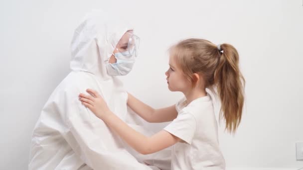 Une petite fille étreint un médecin dans une combinaison de protection blanche, masque, lunettes et gants — Video