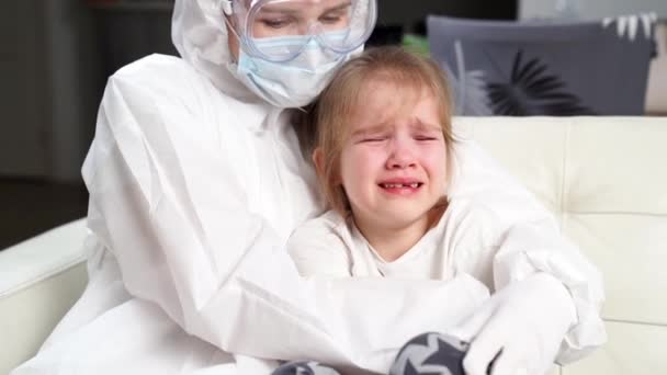 Лікар в захисному костюмі, маска, рукавички та окуляри заспокоює маленьку хвору дівчинку . — стокове відео
