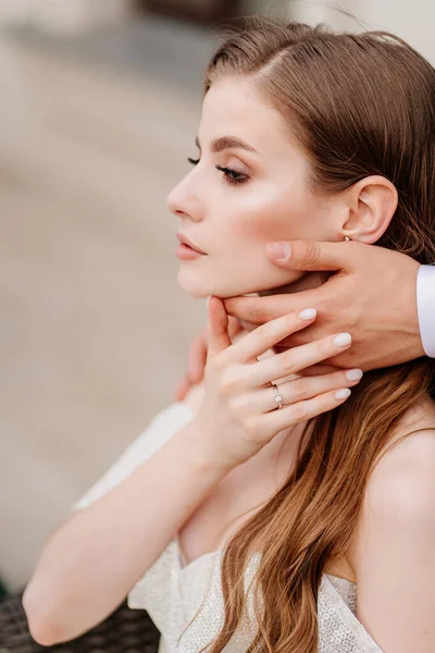 As mãos dos noivos tocam suavemente o rosto da bela noiva. — Fotografia de Stock