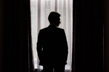 Silüet. Pencerenin yanında ceketli bir adam var. İş adamı. Nişanlı.
